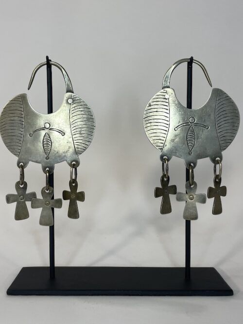 Traditional Mapuche carterita earrings in alpaca silver with engraved decoration and hanging cross pendants displayed on black metal stand.